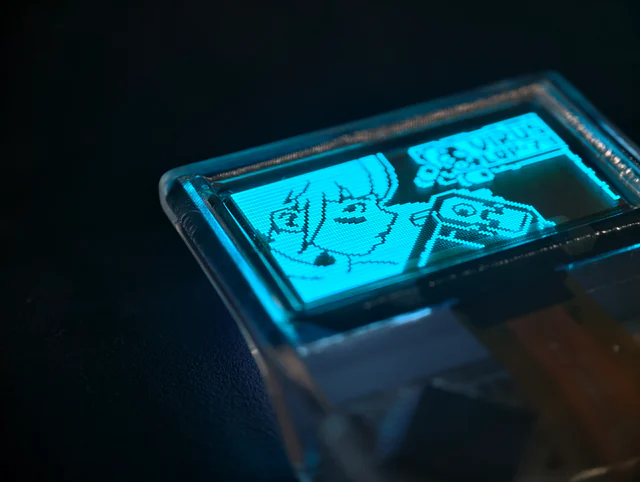 Angled macro photograph of the transparent OLED showing a cyan pixel-art character.